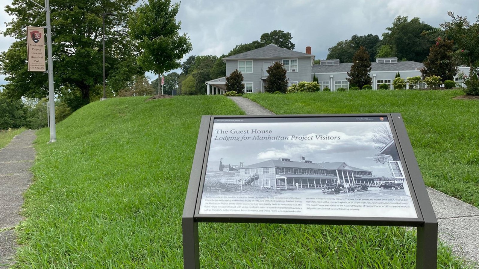 A large gray hotel-type building on a hill with historical marker in foreground