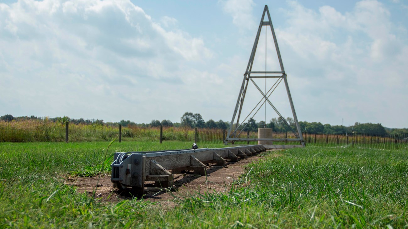 A long wood and steel rail connecting to a pyramid shaped tower in the grassy field