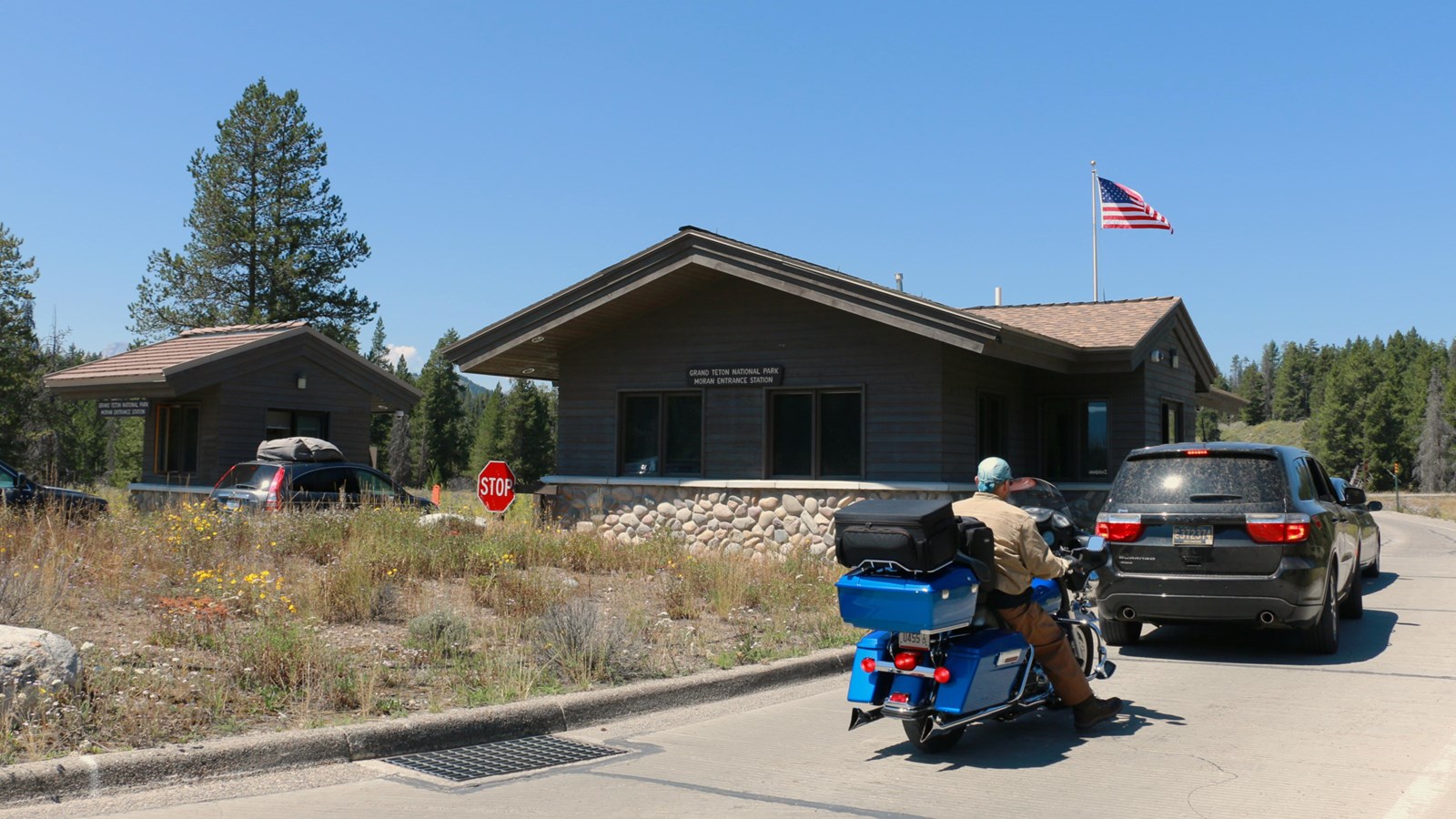 Multiple vehicles and a motorcycle line up outside of two entrance station booths.