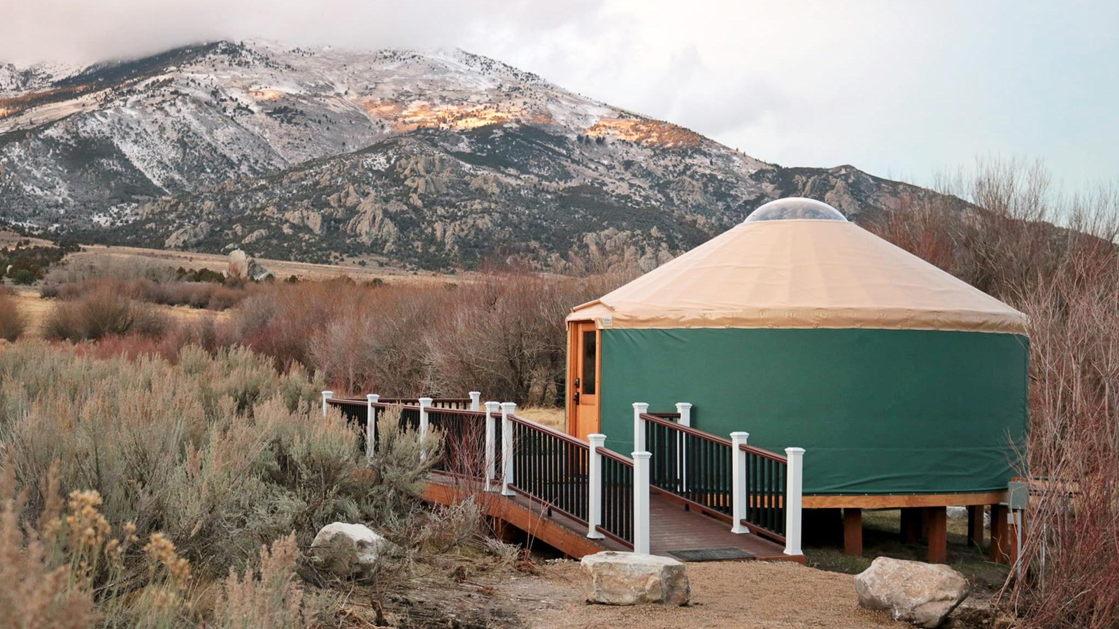 Yurt with deck at sunset with snow capped mountains in the back drop.