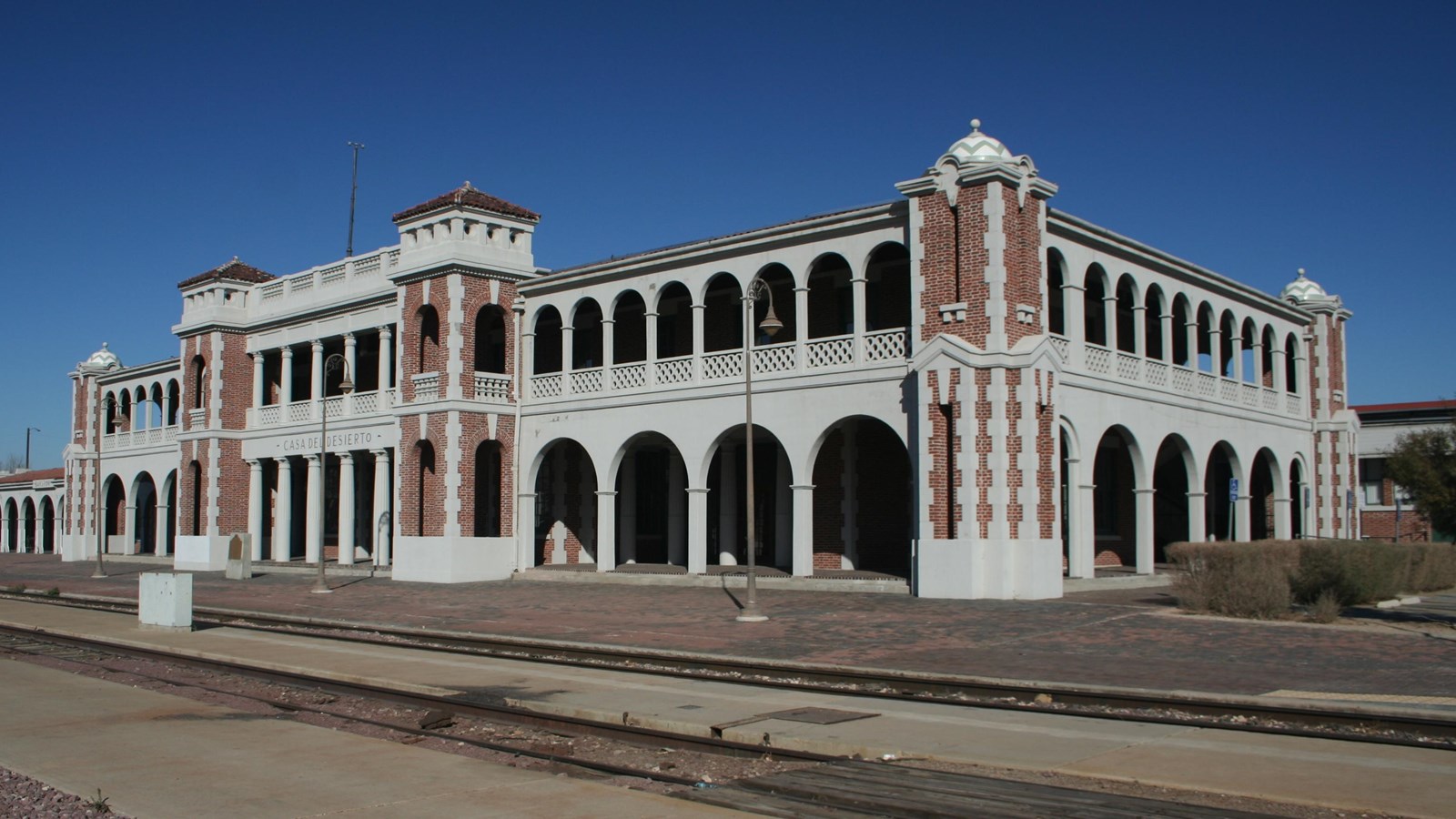 A two story white building with red brick detailing, covered patios supported with arched pillars.