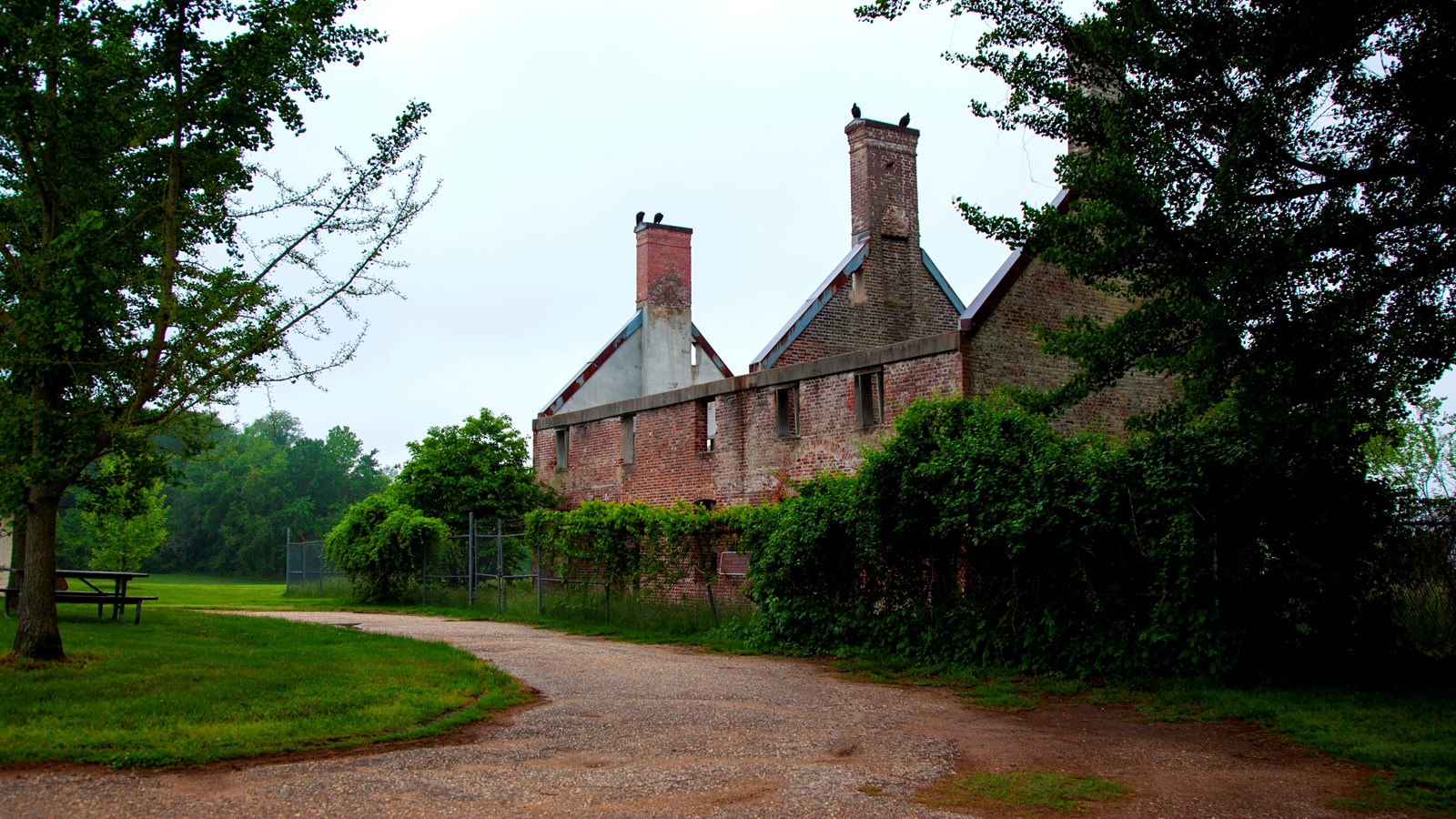 The ruins of a brick house surrounded by a fence and edged by a gravel road