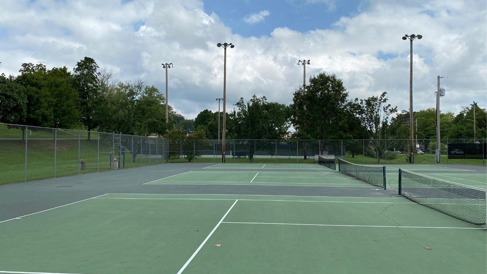 Three green courts with white stripes and three nets all surrounded by chain-link fencing.