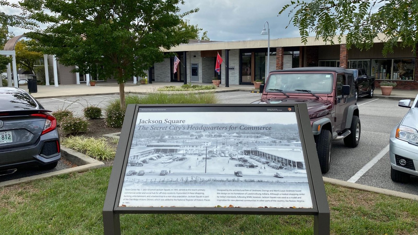 A strip mall with cars parked and historical marker in foreground