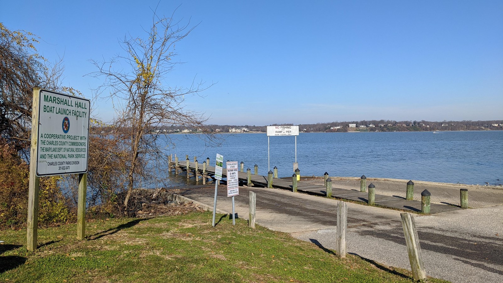 A concrete boat ramp leads to a river. A sign to the left reads \'Marshall Hall Boat Launch\'