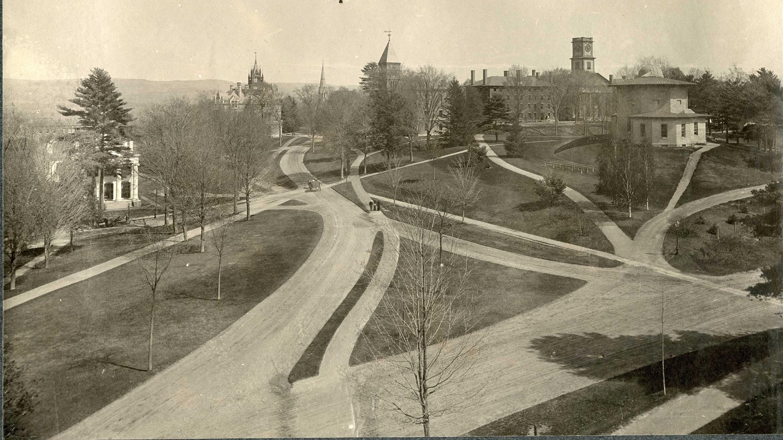 Black and white of curving paths with trees spread out leading to buildings. 