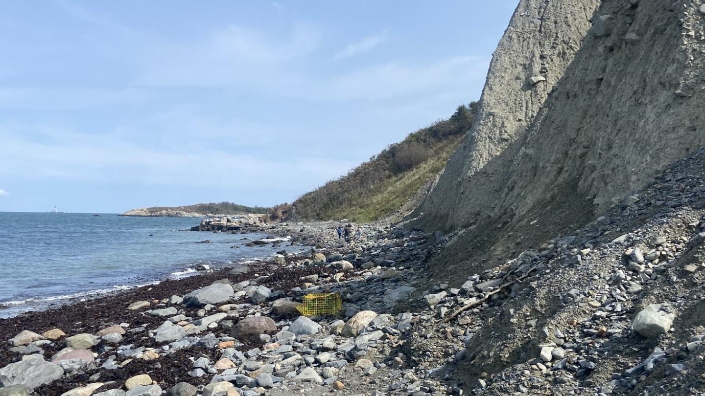 Shoreline of Great Brewster. The beach is rocky, water is on the left. Bluffs on the right.t