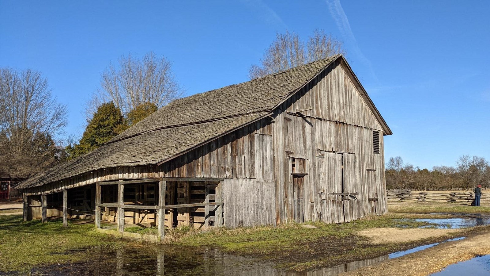 A weathered wooden barn with an overhang covering animal pens