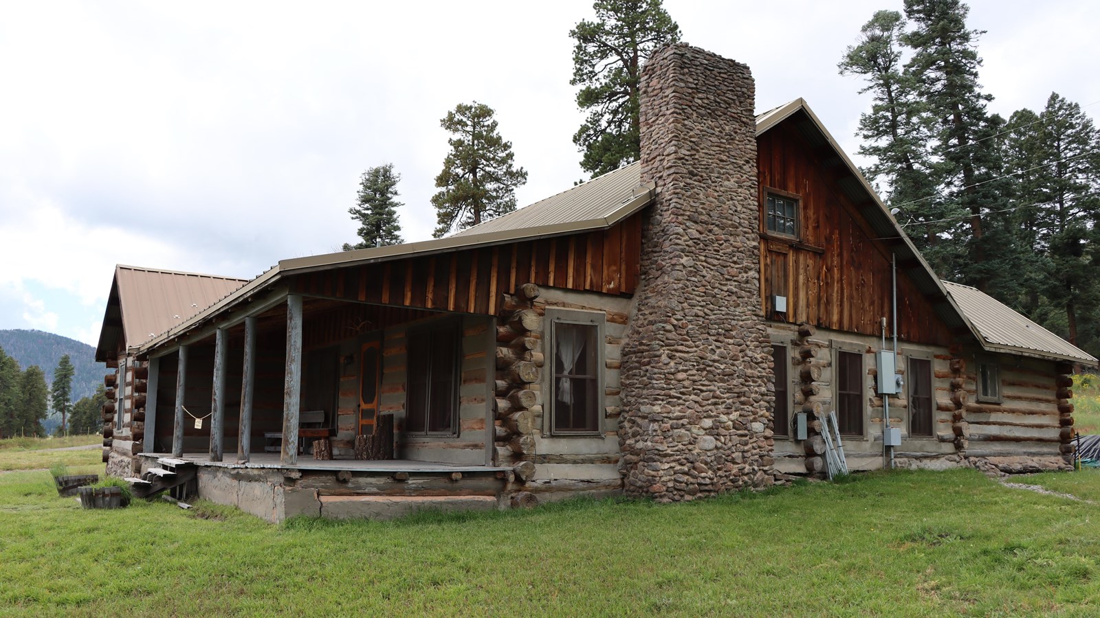 A historic log cabin with stone chimney at the edge of a pine grove