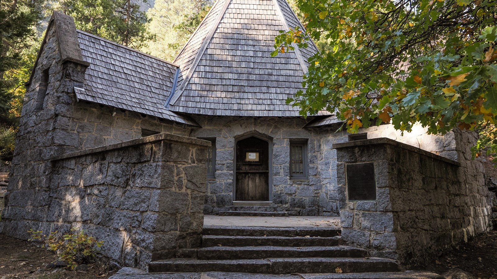 A rustic stone building with a central peak and gabled roofs on either side
