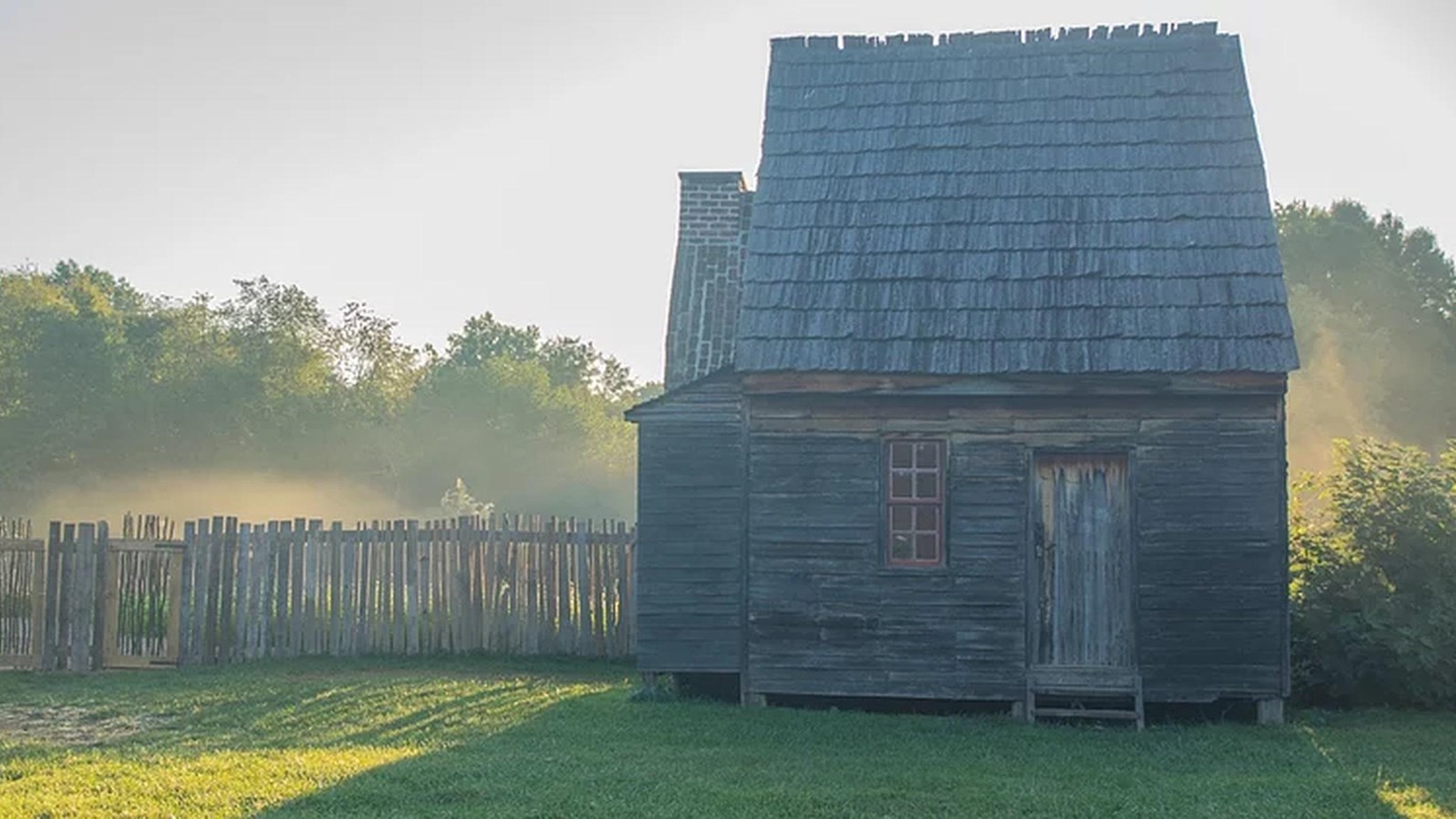 A small one room house with weathered wood siding and a chimney on the side