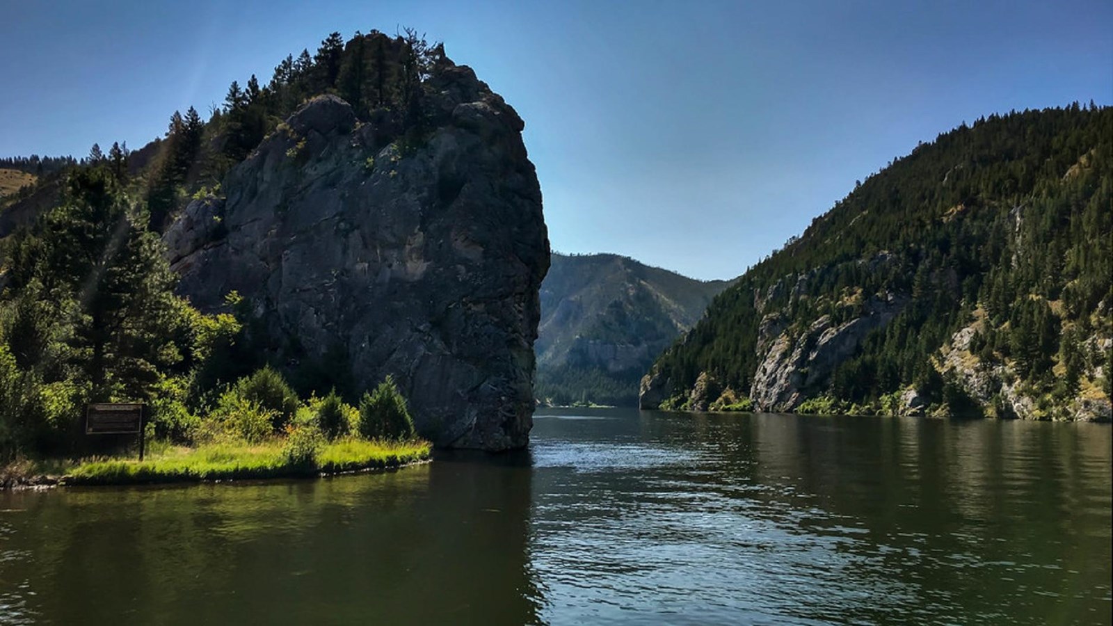 a calm river winds between two large rock outcroppings covered in trees.