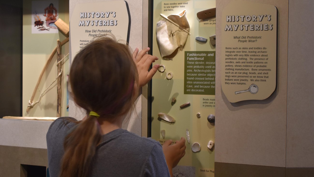A child with long hair looks into a display of shell artifacts