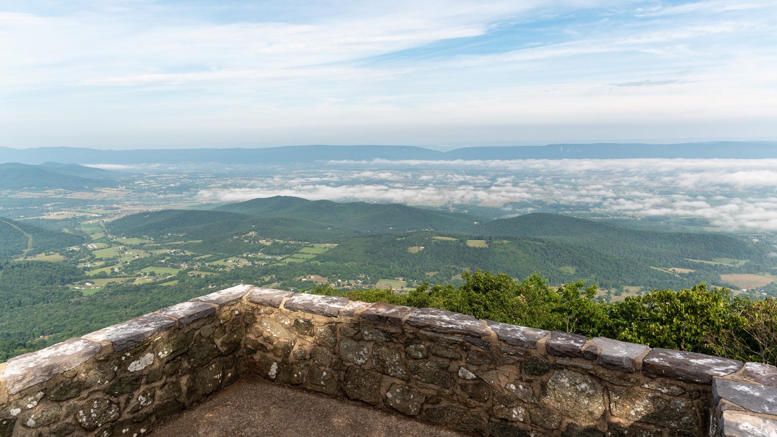 A stone platform with a view of a valley below and blue mountains beyond.