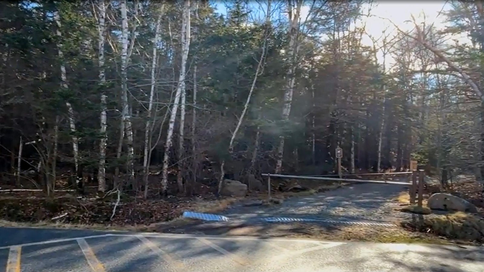 The edge of an asphalt parking lot with faded paint lines with a metal gate across a gravel side roa