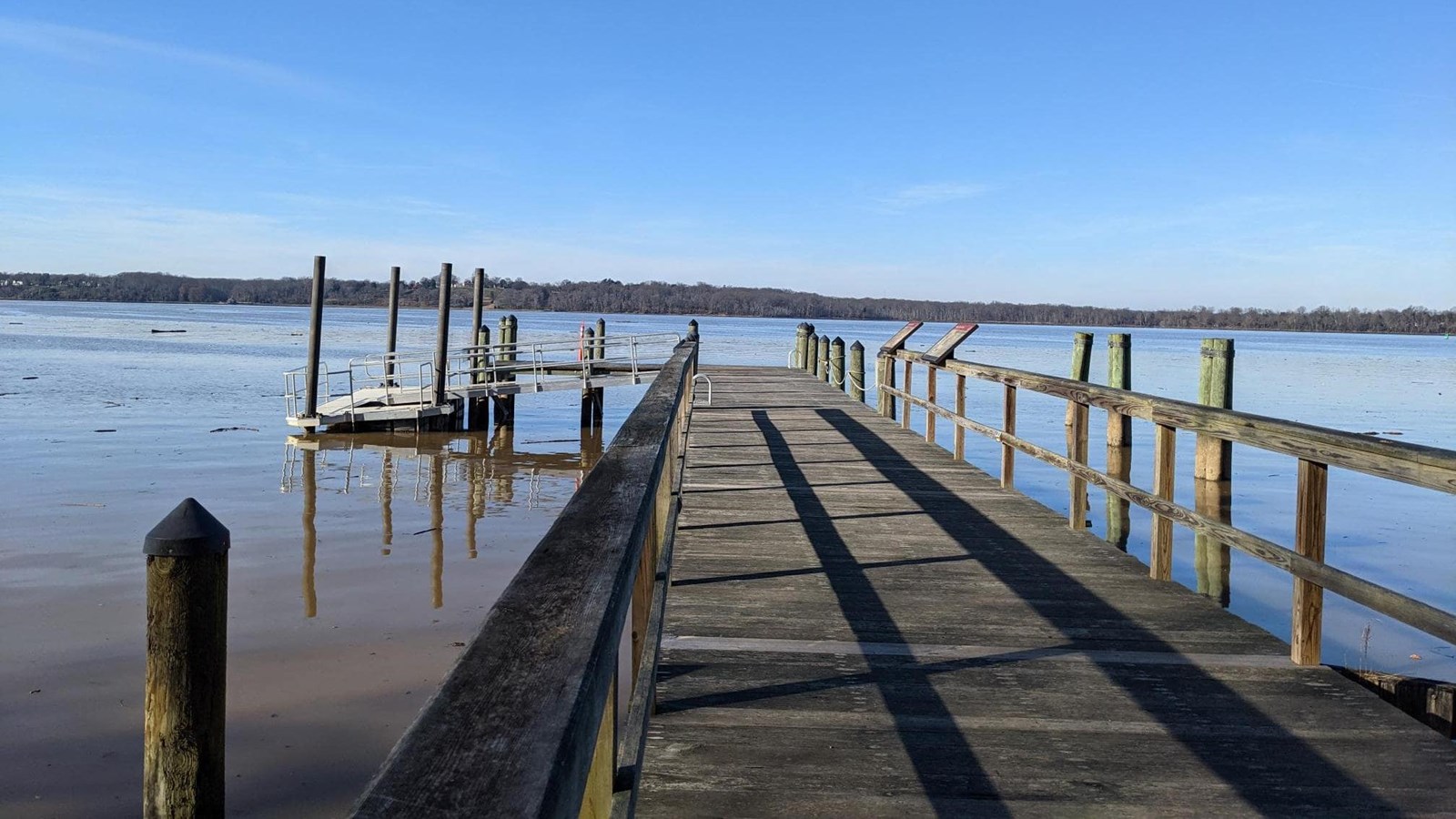 A wooden dock extends over blue water. A small floating dock is attached to the end.