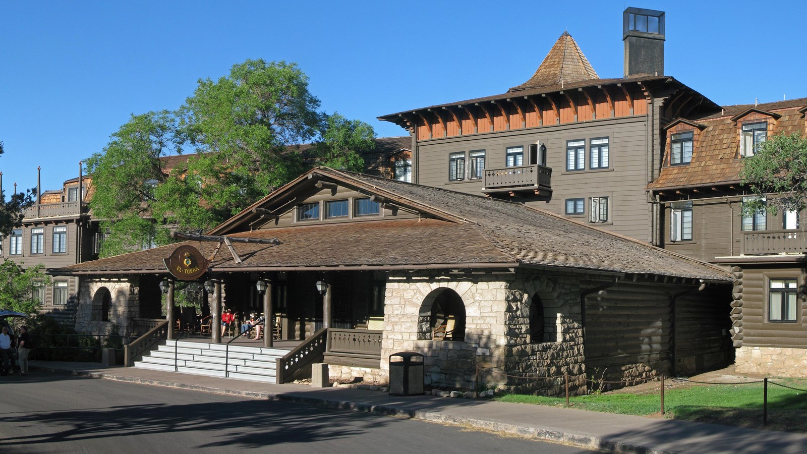 A large, multi-story wooden building features a tall turret and a wide, covered front porch.