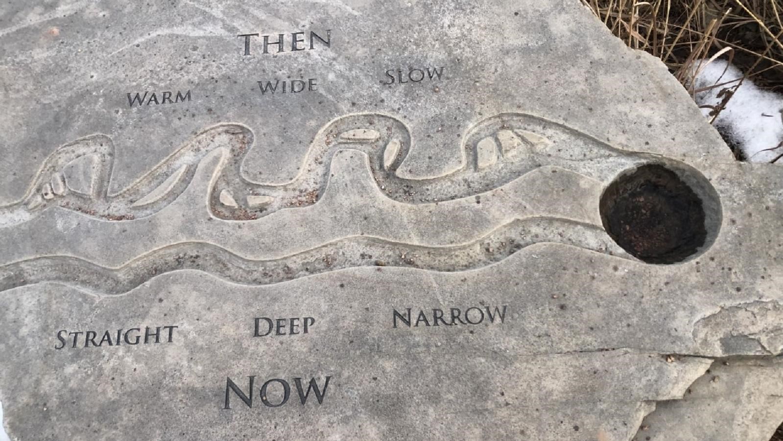 A large flat tan and gray rock with jagged edges. Words and channels have been carved into the rock.