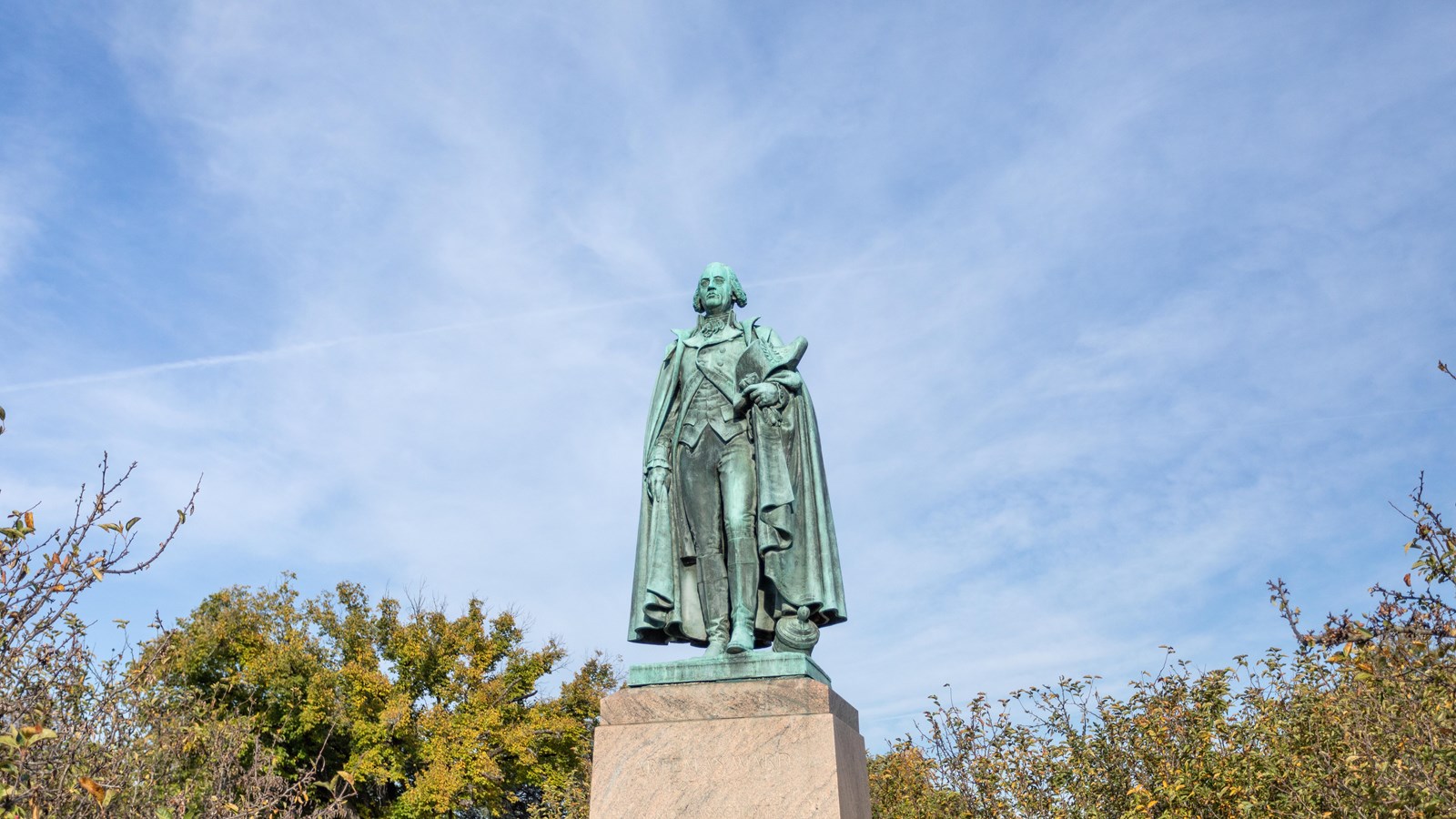 A large green statue of a man wearing a cape. 