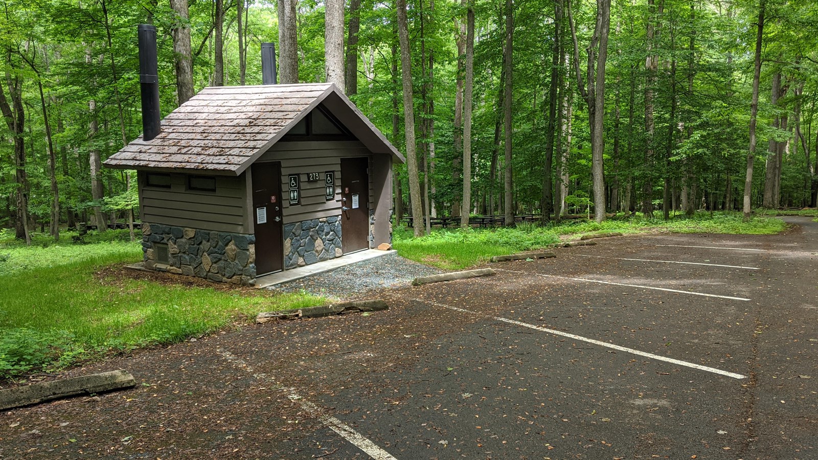 Brown building by parking area with two doors. The doors are labeled with restroom signs. 