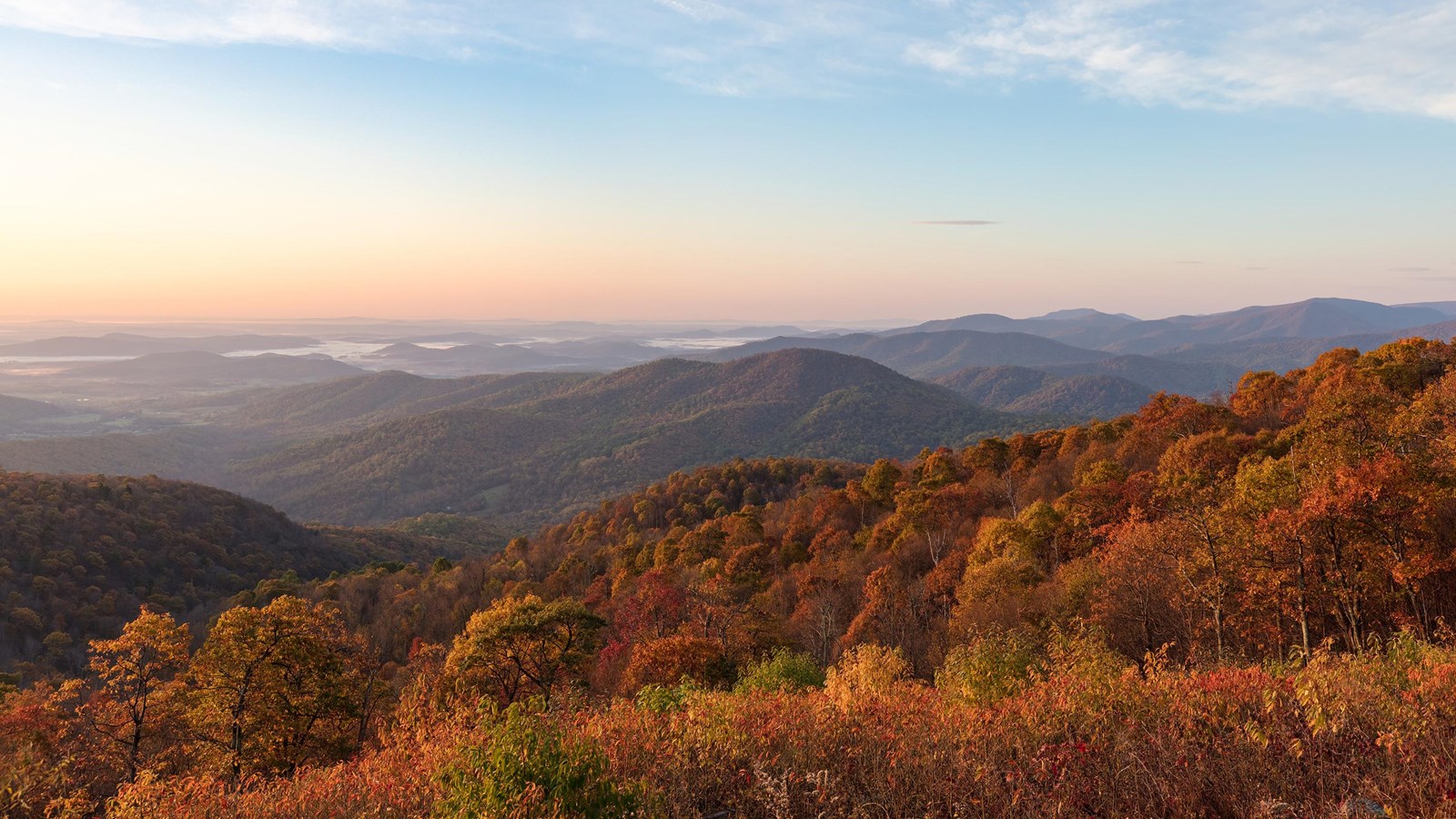 A view from an overlook down into a valley below filled with fall colors of red and orange.