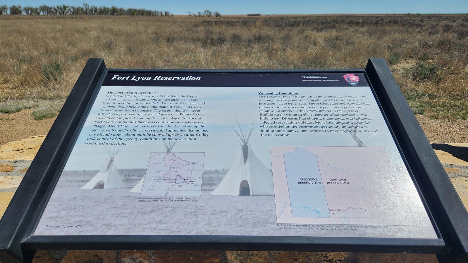 A wayside in a stone base with open prairie beyond, and a line of trees in the distance