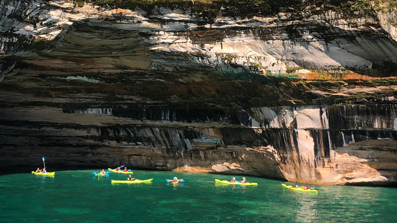 Group of yellow kayaks next to colorful cliff