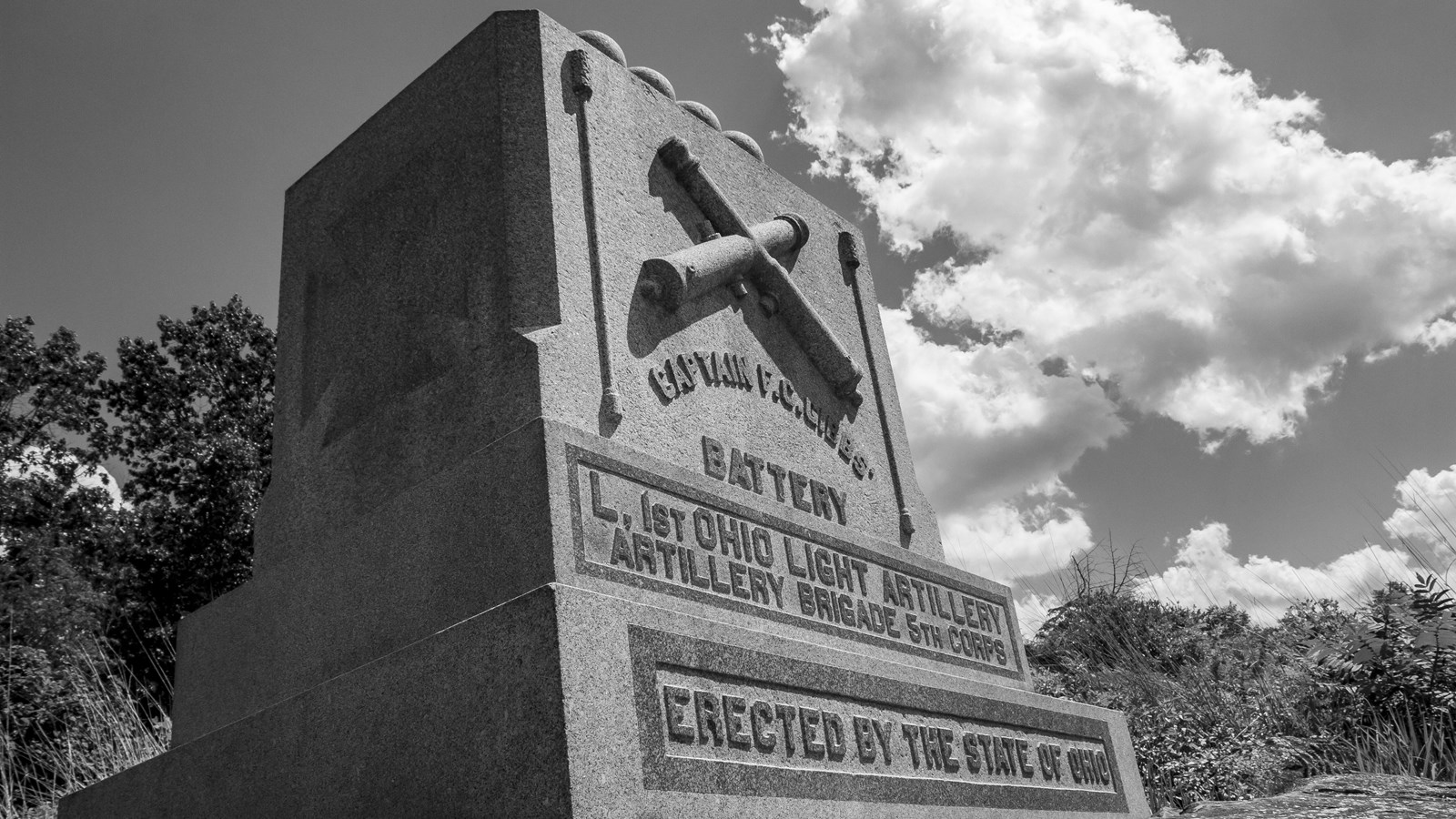 A black and white image of a stone monument with crossed artillery pieces