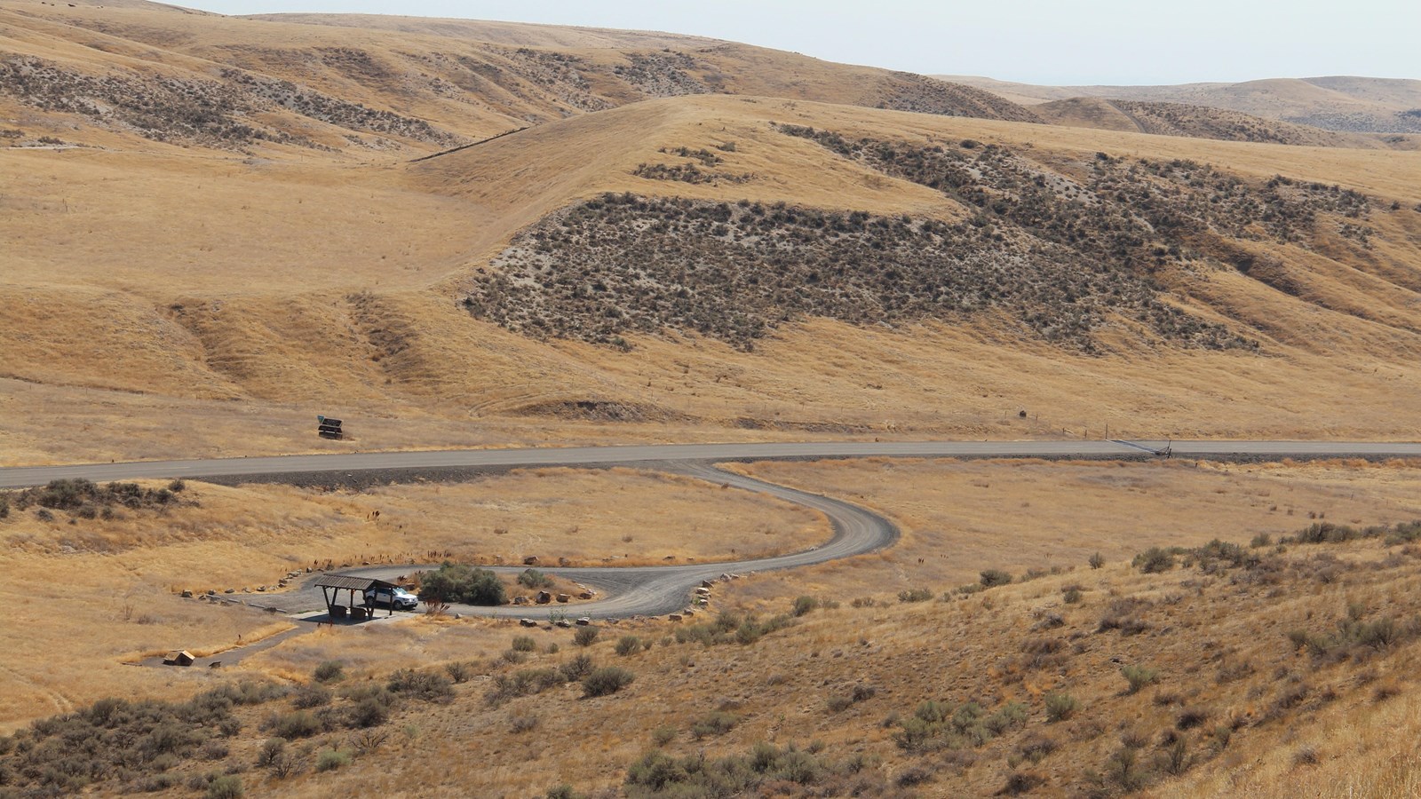 Rolling field with hills and a road through it from the middle left to the middle right of the image