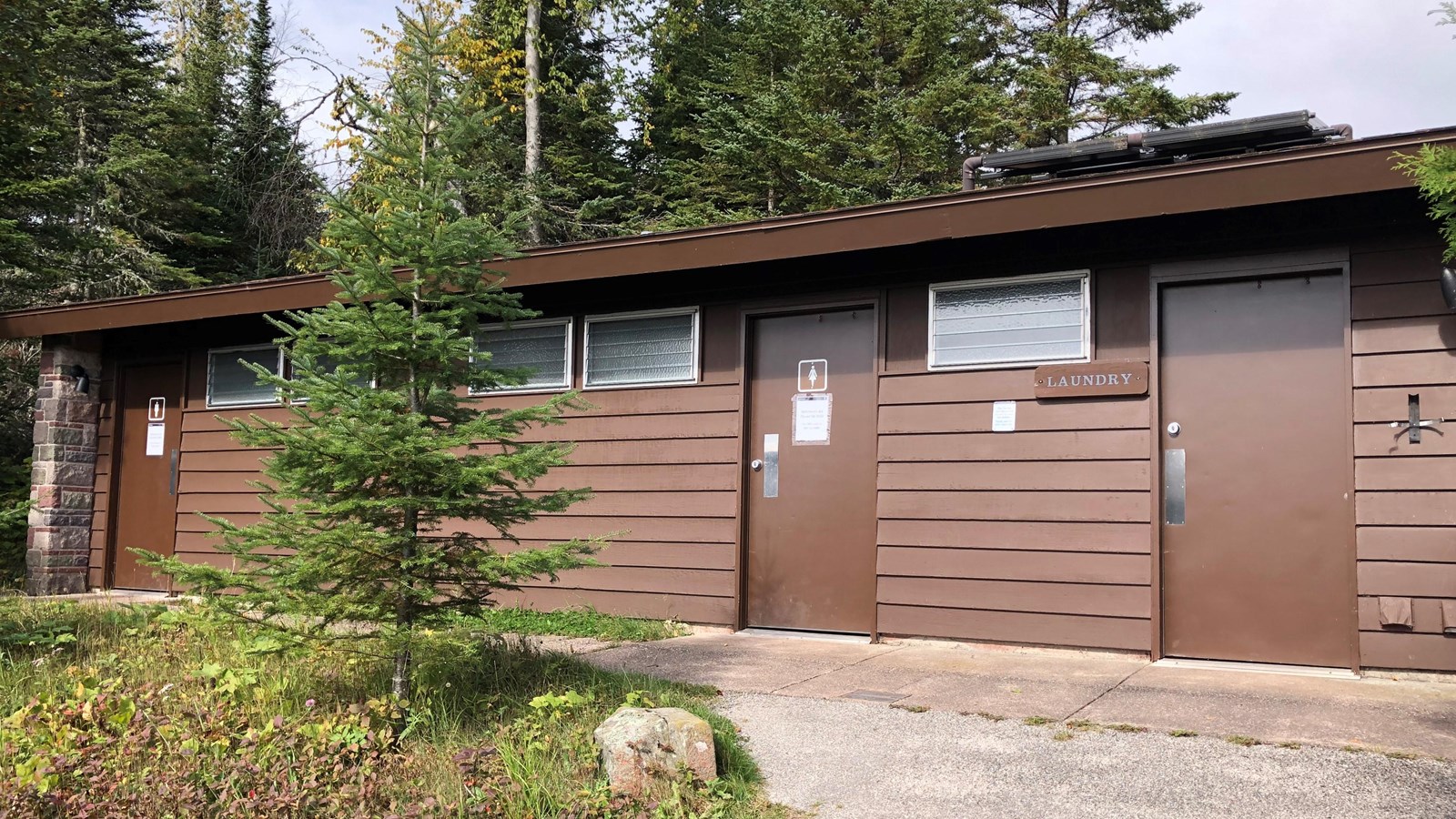 A paved path leads to a bathroom building surrounded by trees. 