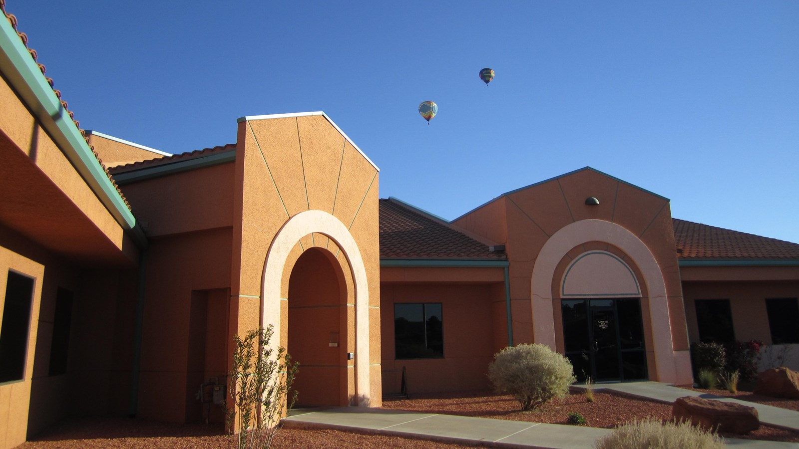 Tan and blue building with arches over the doorways. An American flag flies at half staff.