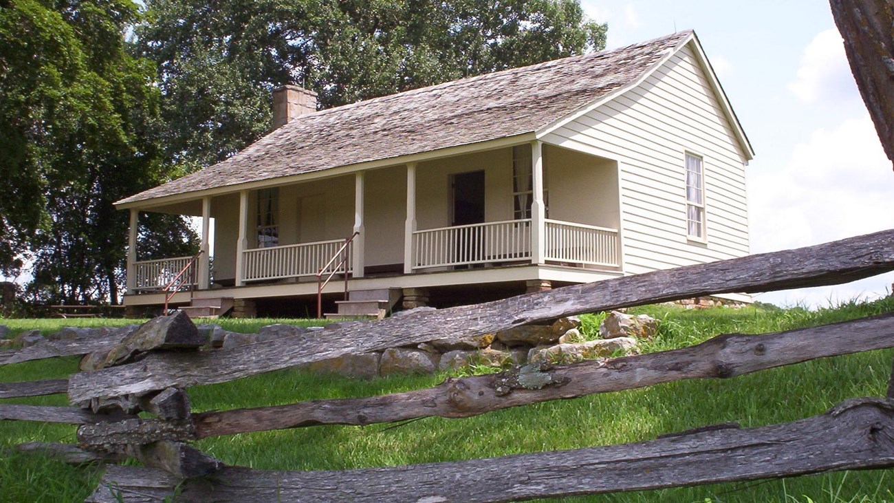Ray House in the summer with split rail fencing at the border of yard in front of wire road path