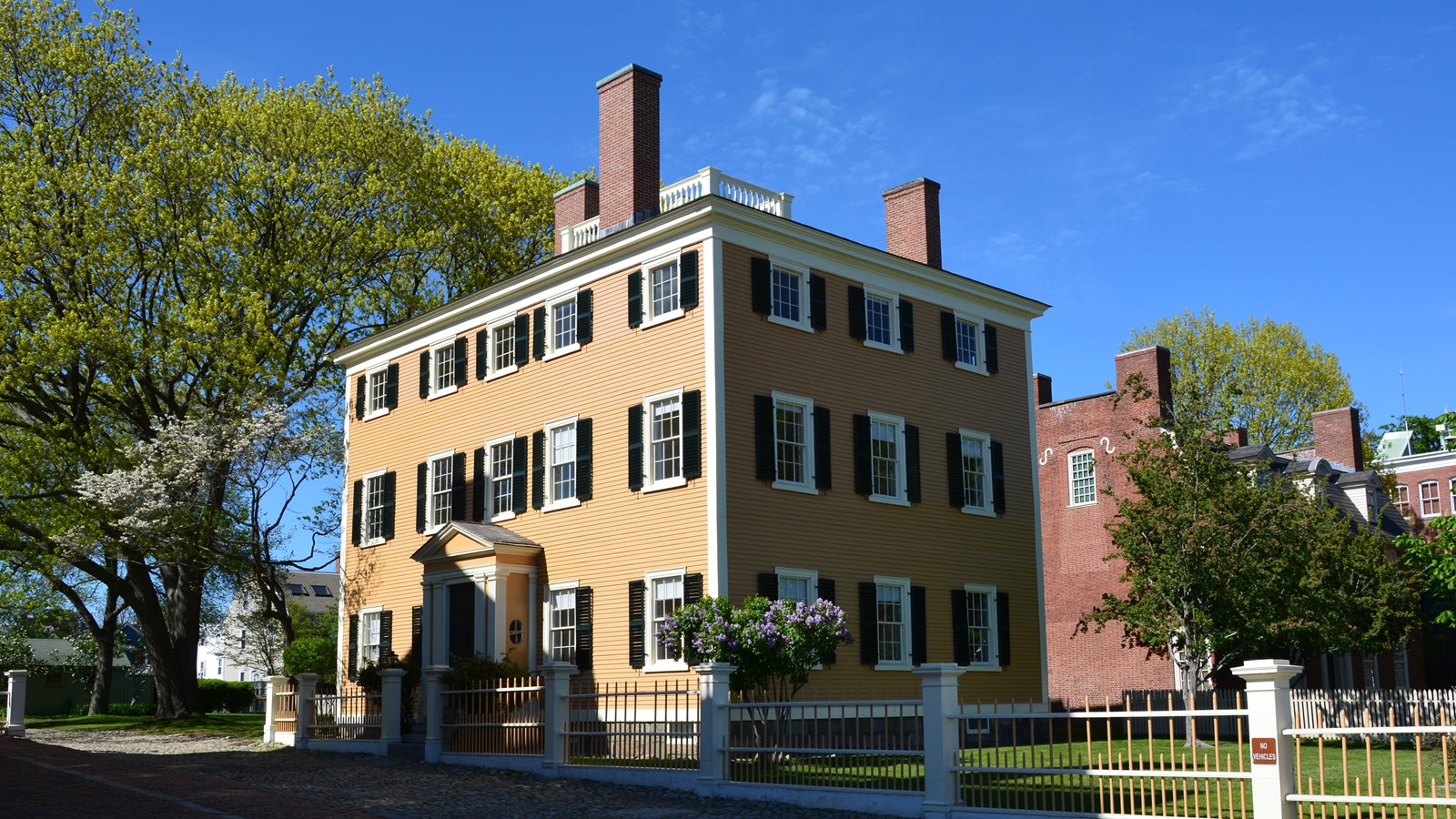 Square, three story yellow federal style home with white trim and green shutters