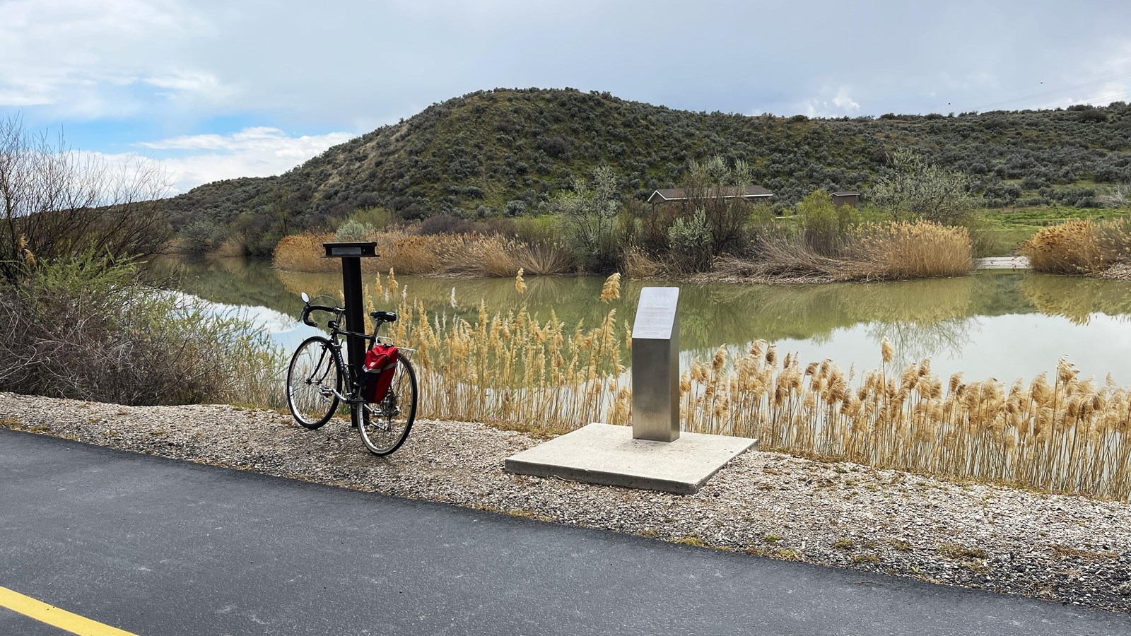 A bicycle leans against a t-shaped marker above a river. A post is to the right.