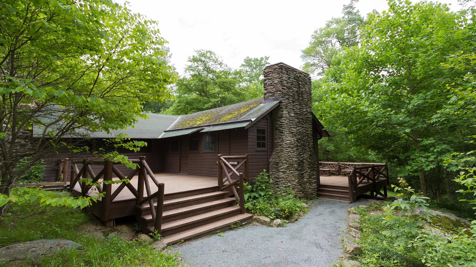 An historic wood cabin with a large porch sits in the middle of a forest.