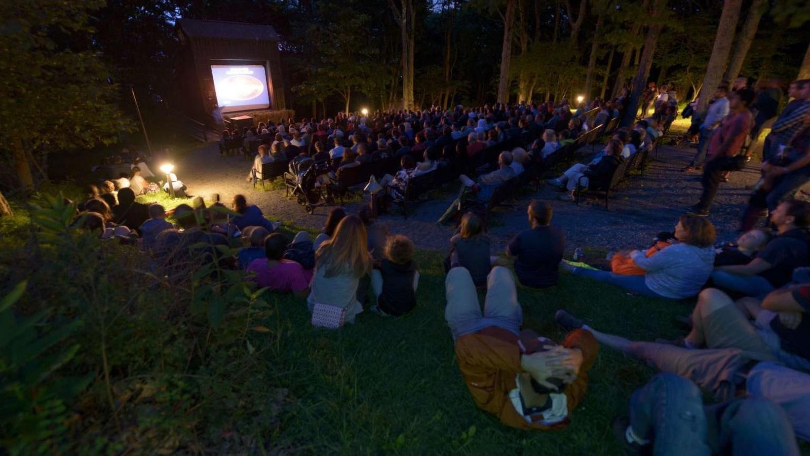 A color photograph of people sitting in an amphitheater watching an evening program.