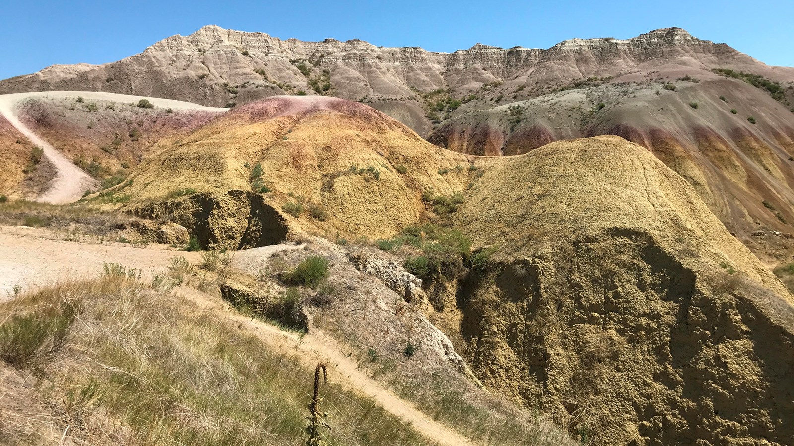 A small trail proceeds through rolling mounds of striped colors: yellows, reds, whites, browns.