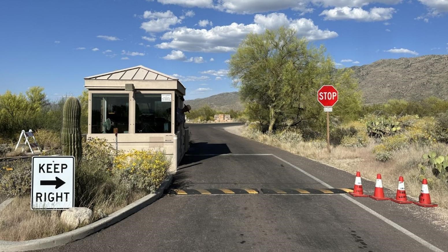 A ranger sticks their head out the window of a kiosk in the median of a road next to a stop sign