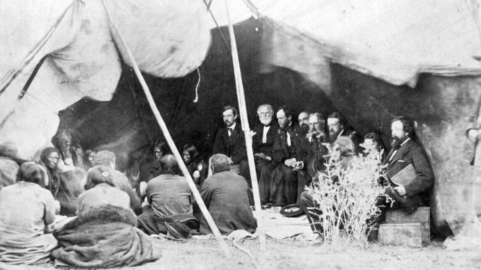 A tent covers several tribal leaders and several soldiers all sitting a circle formation