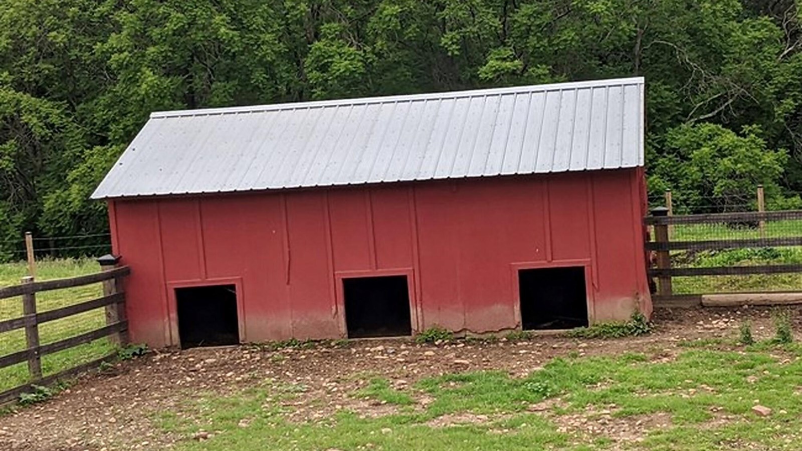 A small red building with a metal roof. Three small square openings sit at the bottom.
