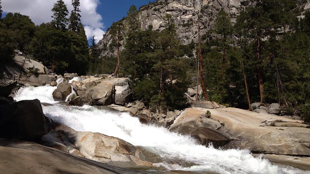 A cascading waterfall with massive granite mountains in the background.