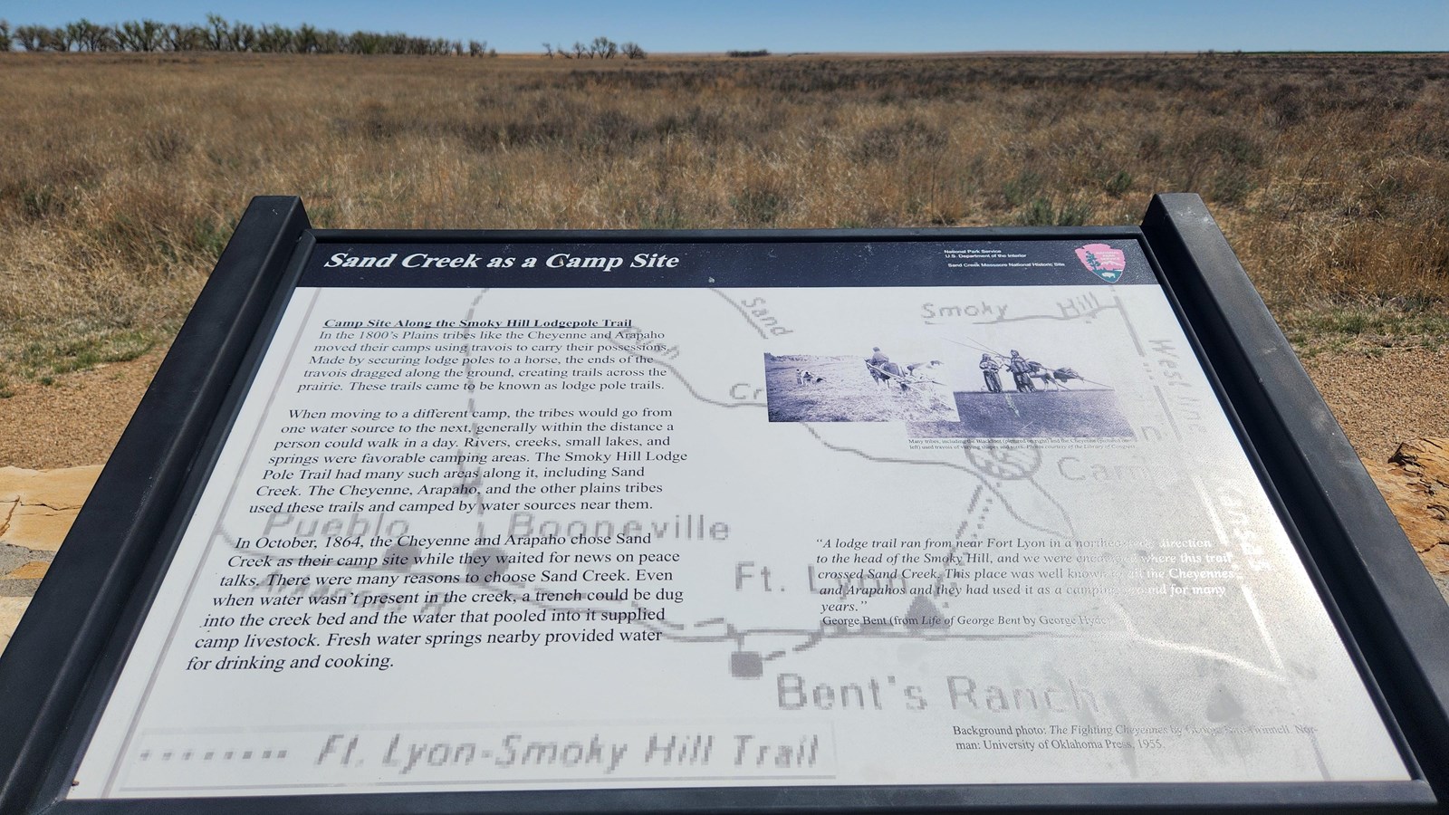 A wayside in open prairie with a line of trees in the distance