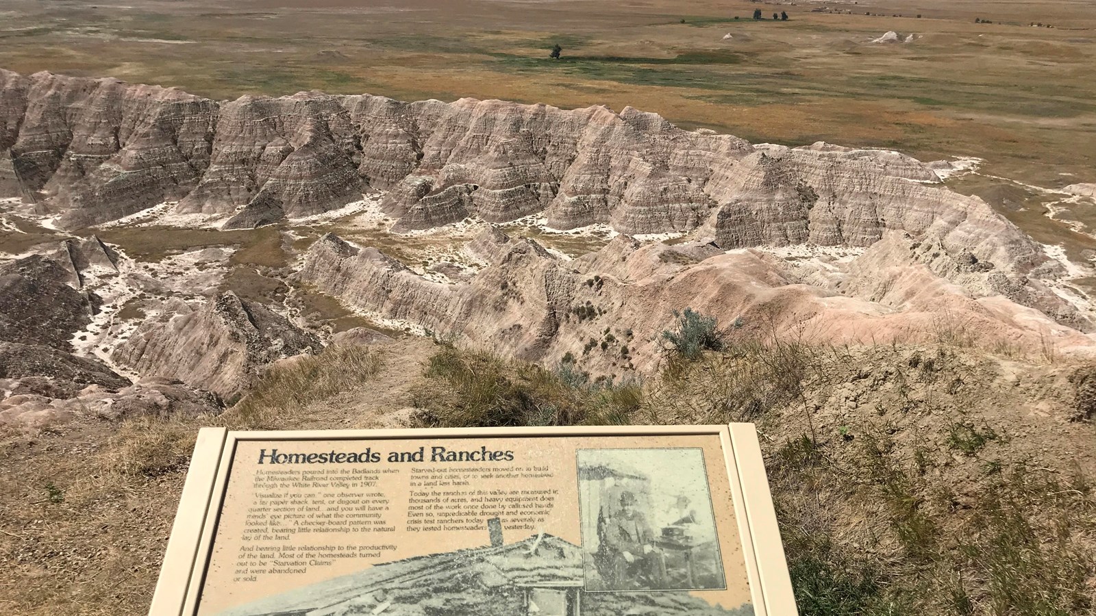 A wayside exhibit discussing homesteading lies in front of a view of badlands canyons and prairie.