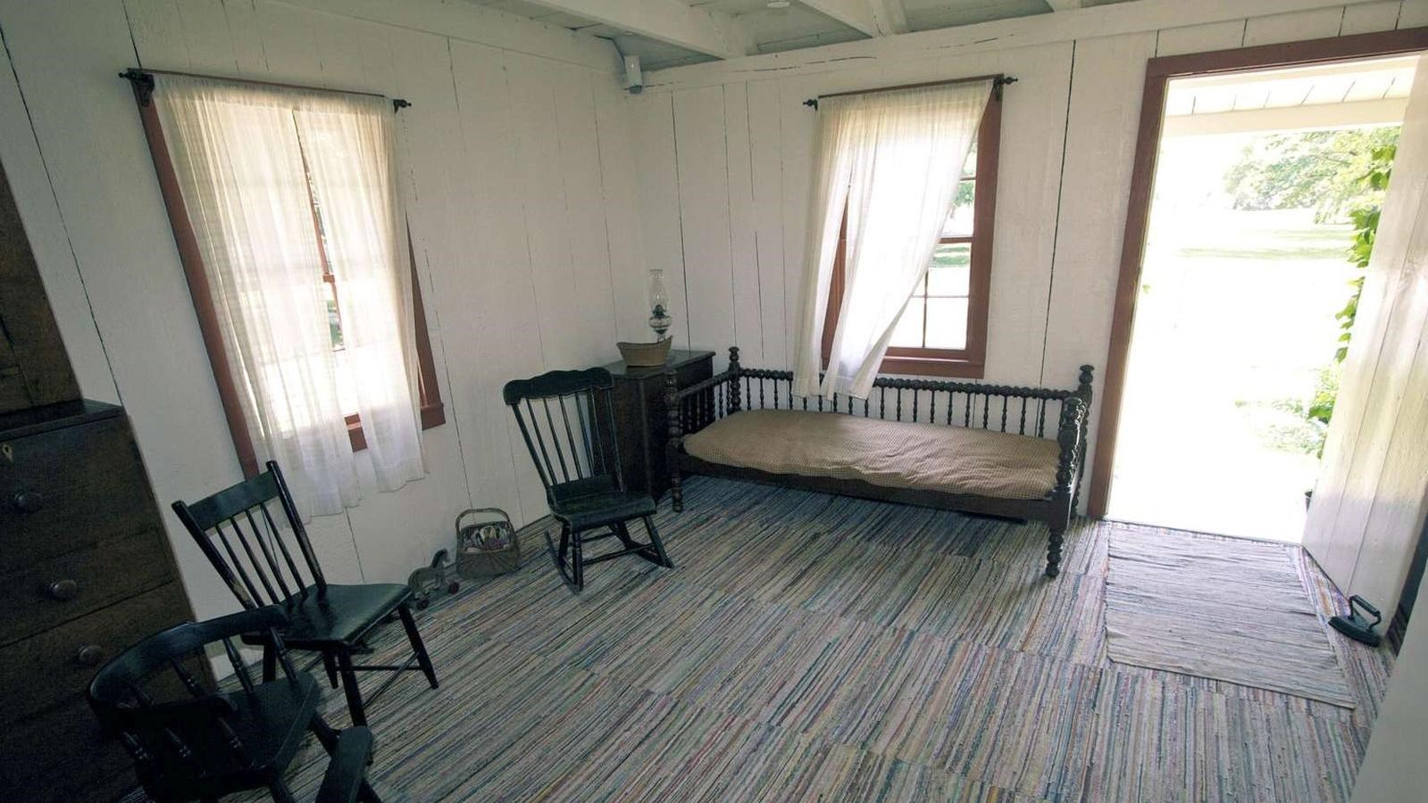 A rag rug carpeted room is furnished with wooden chairs and a day bed.