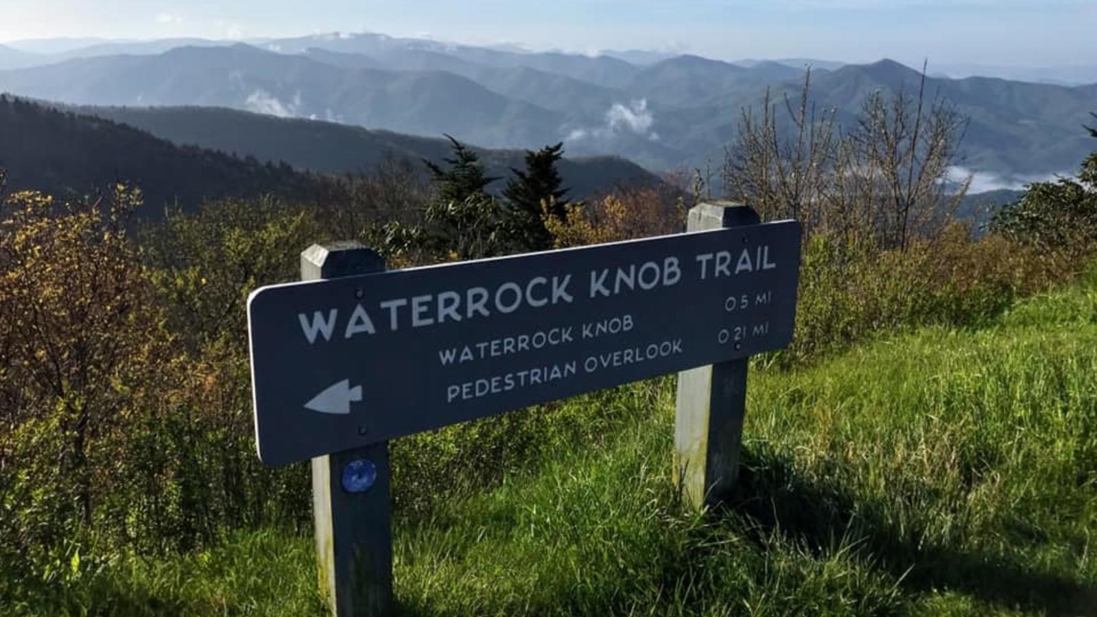 Wooden sign reading Waterrock Knob Trail with rolling mountains in distance