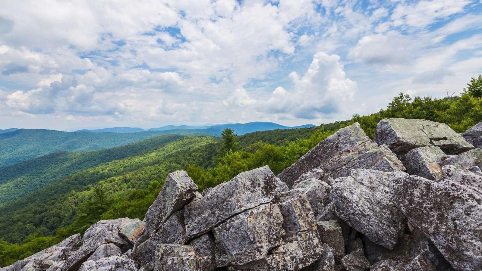 A color photograph of a rocky talus slope facing out to lush green mountains in the distance.  