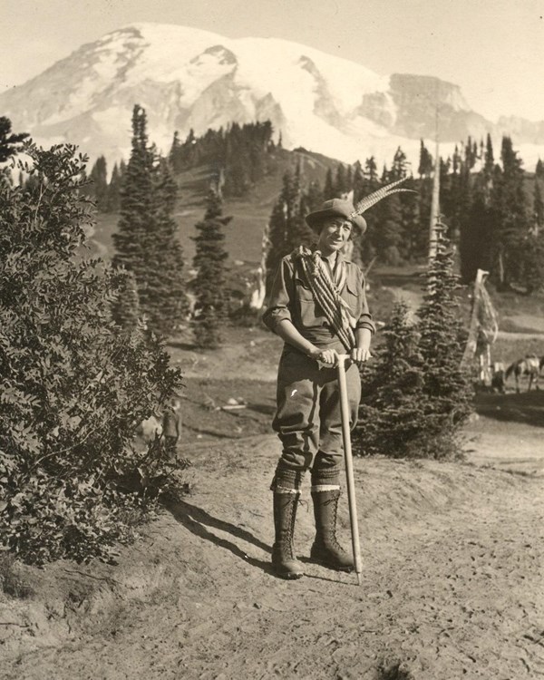 Historic photo of a woman in front of Mount Rainier with ice axe and coil of rope over her shoulder