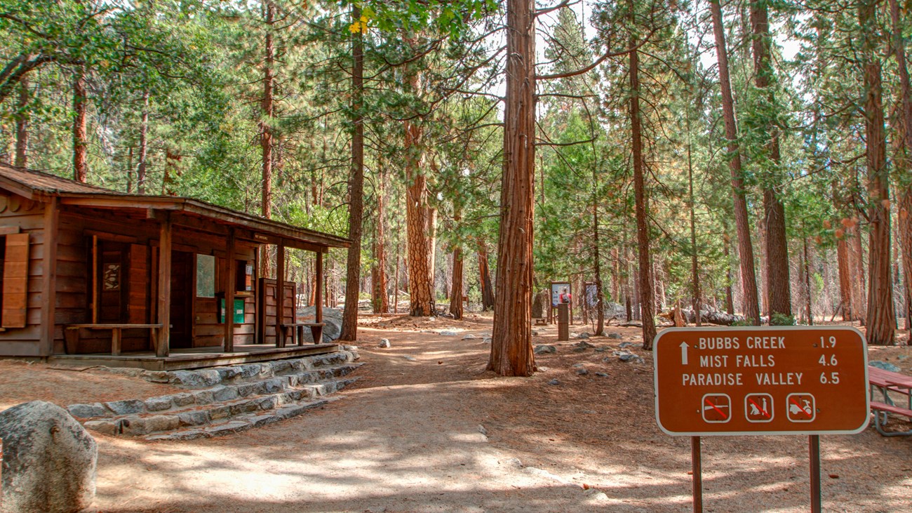 A ranger station next to a trail leading into a forest.