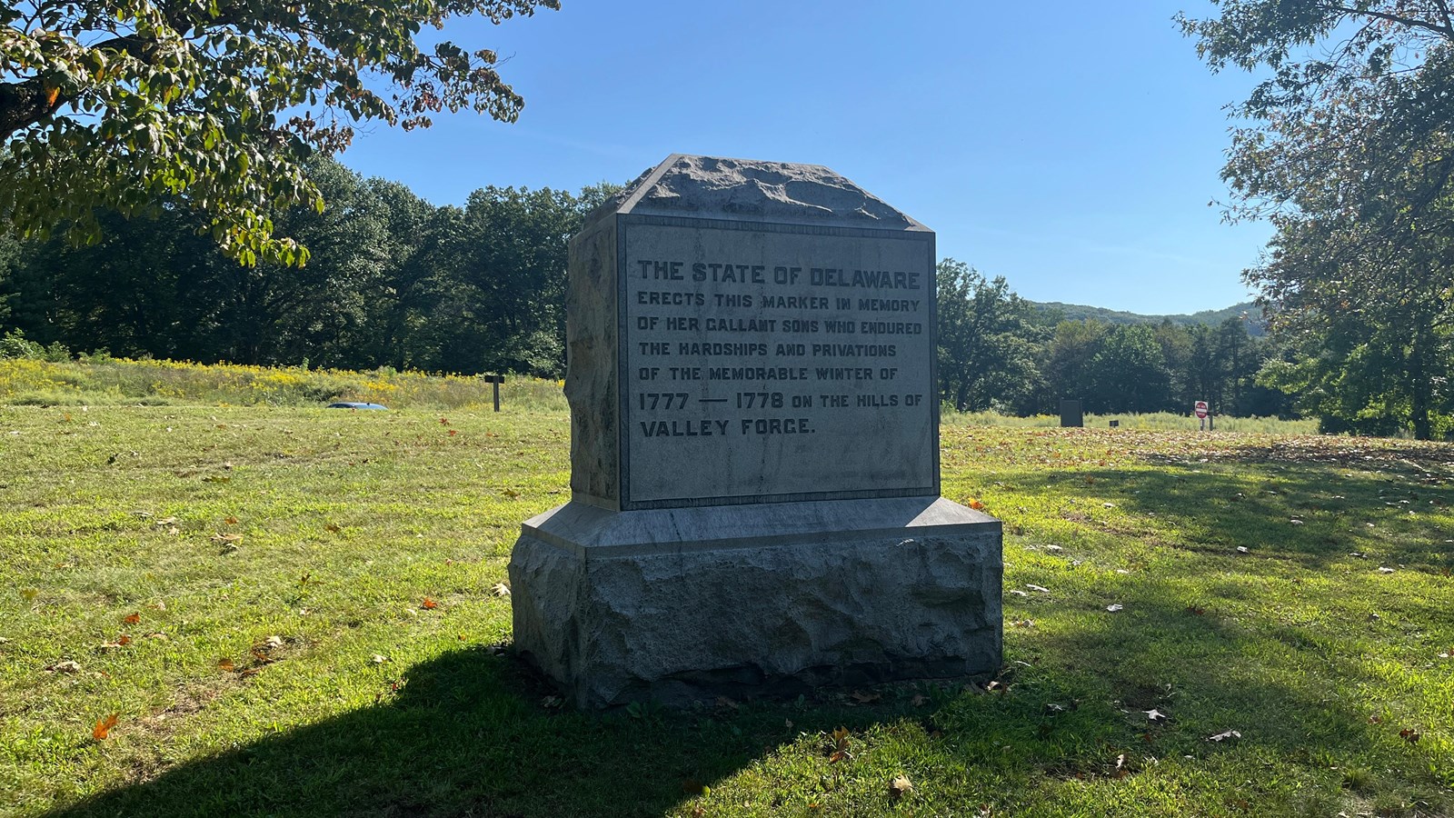 A stone obelisk, rough-hewn around the base and top, containing an inscription in raised stone.