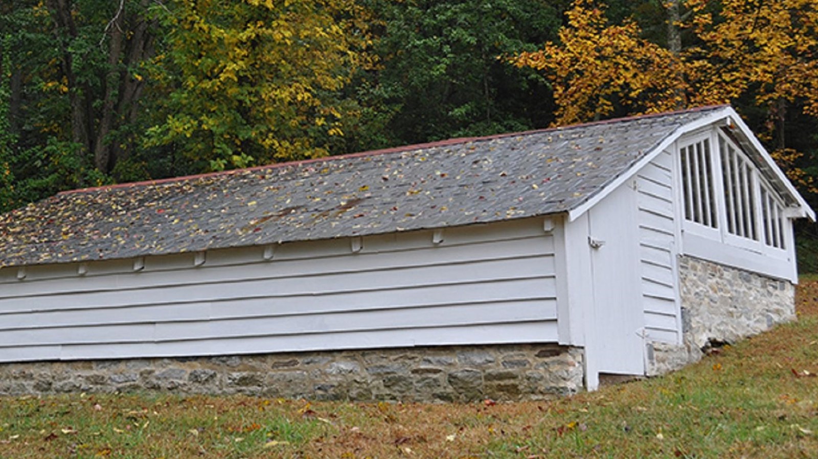 A long white low building with a solid rood on one side and a glass roof on the other.